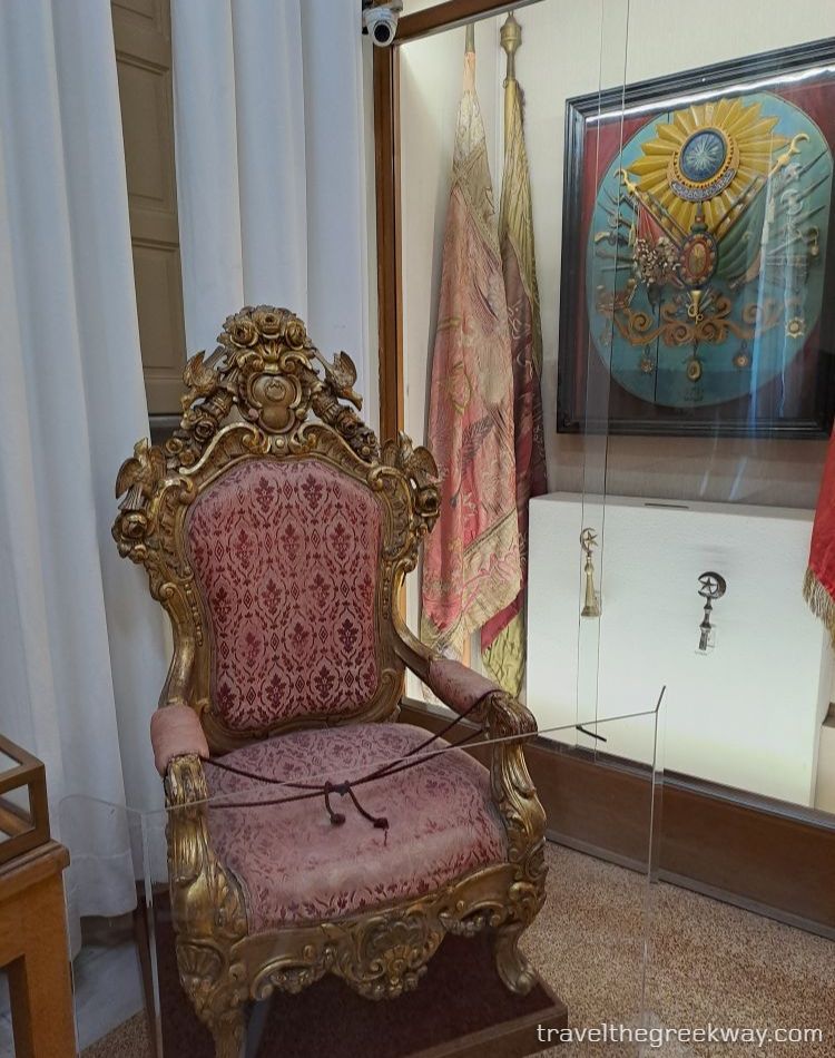 Ornate gilded throne with red upholstery on display at the National Historical Museum of Athens.