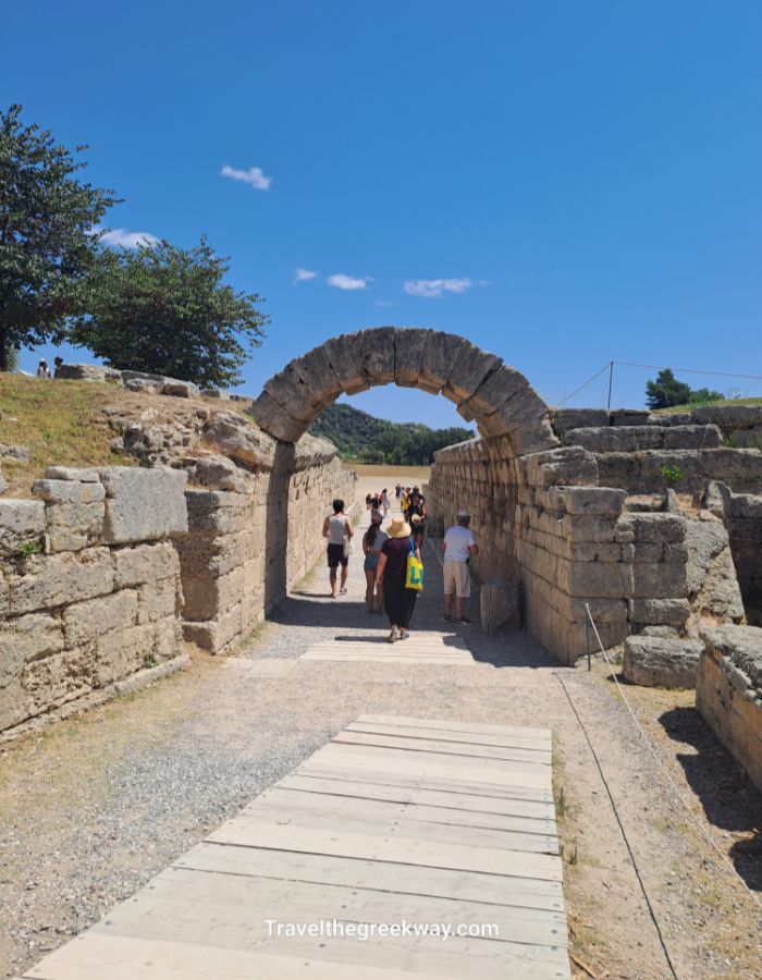 Visitors walking through the ancient stone archway into Olympia’s stadium.