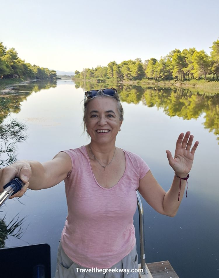 Smiling Evgenia taking a selfie at Kaiafas Lake with trees reflected in the water.