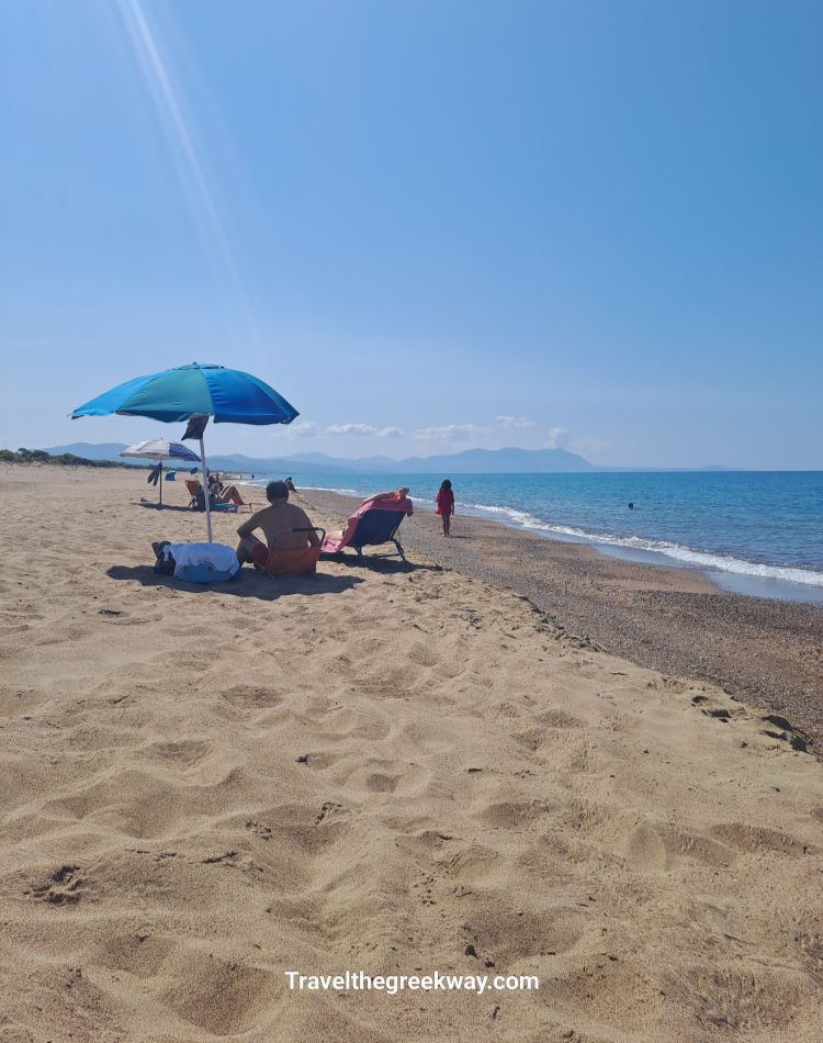 Sandy Kaiafas Beach with people relaxing under umbrellas by the sea.