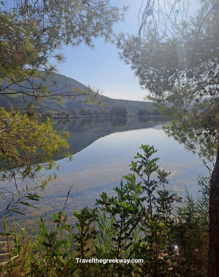 Calm Kaiafas Lake surrounded by trees and reflecting mountains.