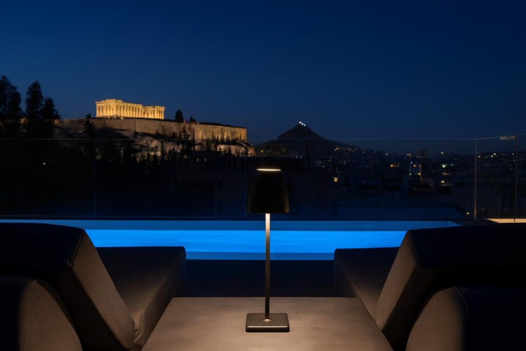Night rooftop pool in Athens overlooking the Acropolis and Lycabettus Hill.