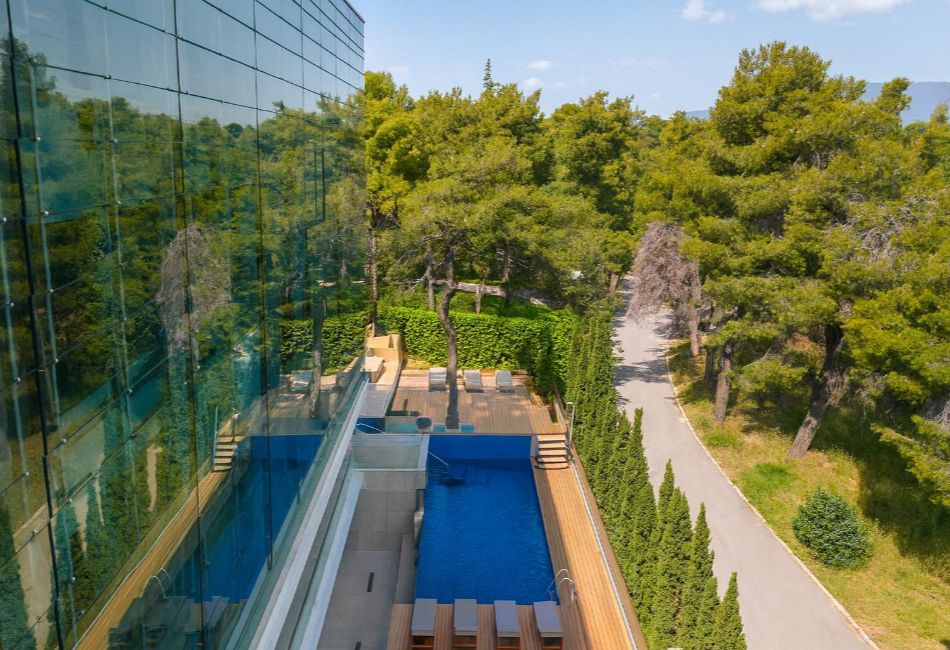 Modern Athens hotel pool by glass building surrounded by pine trees in Ekali.
