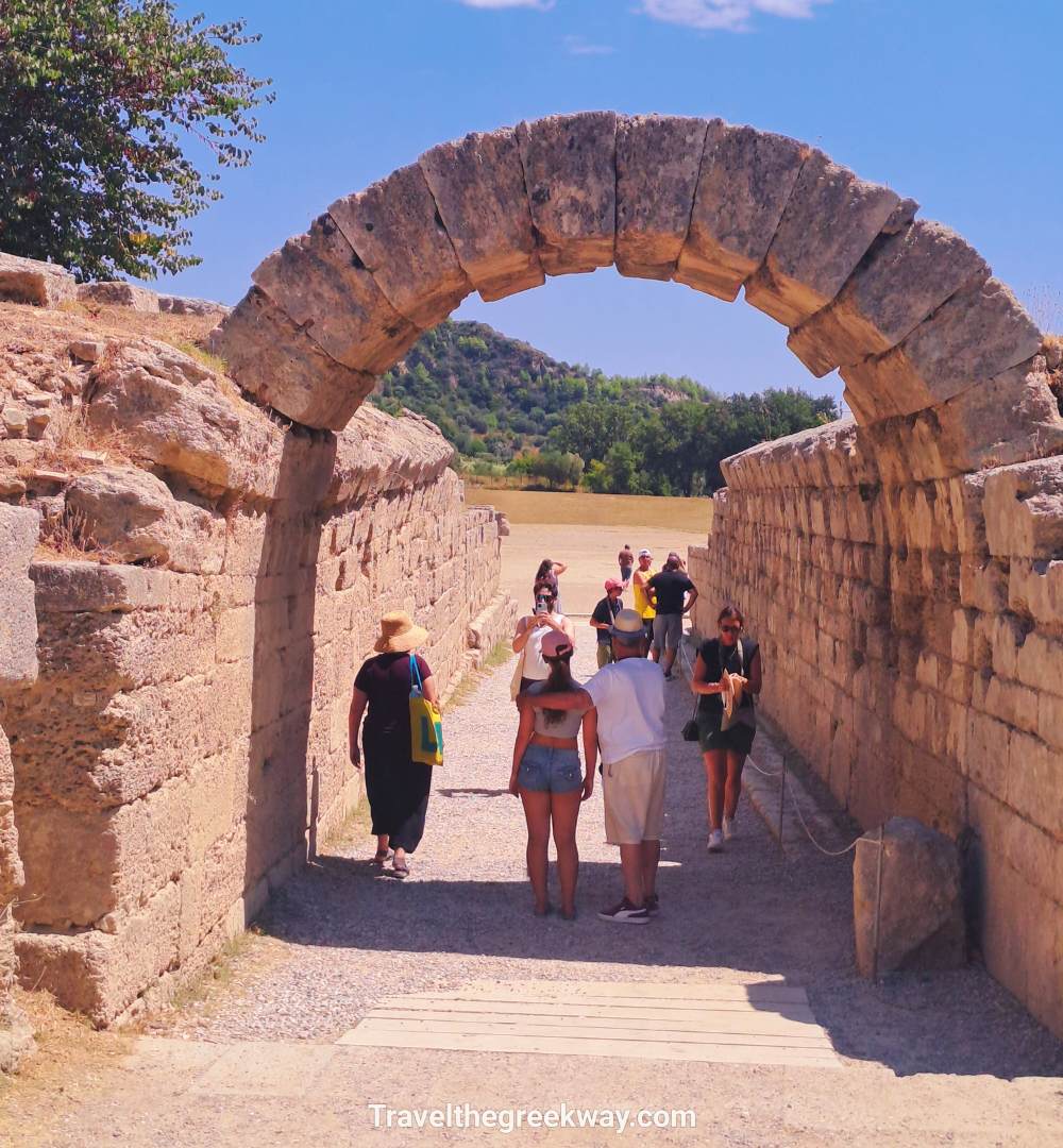 Travelers walking through the ancient stone archway leading into the original Olympic Stadium at the Ancient Olympia site.
