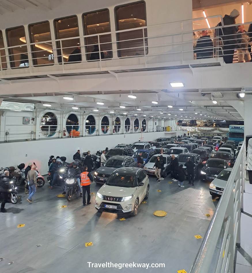 Interior view of a large Greek ferry garage packed with cars, motorcycles, and passengers preparing to disembark.