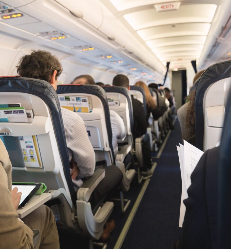 Interior of a commercial airplane cabin showing passengers seated in rows and a view down the center aisle.