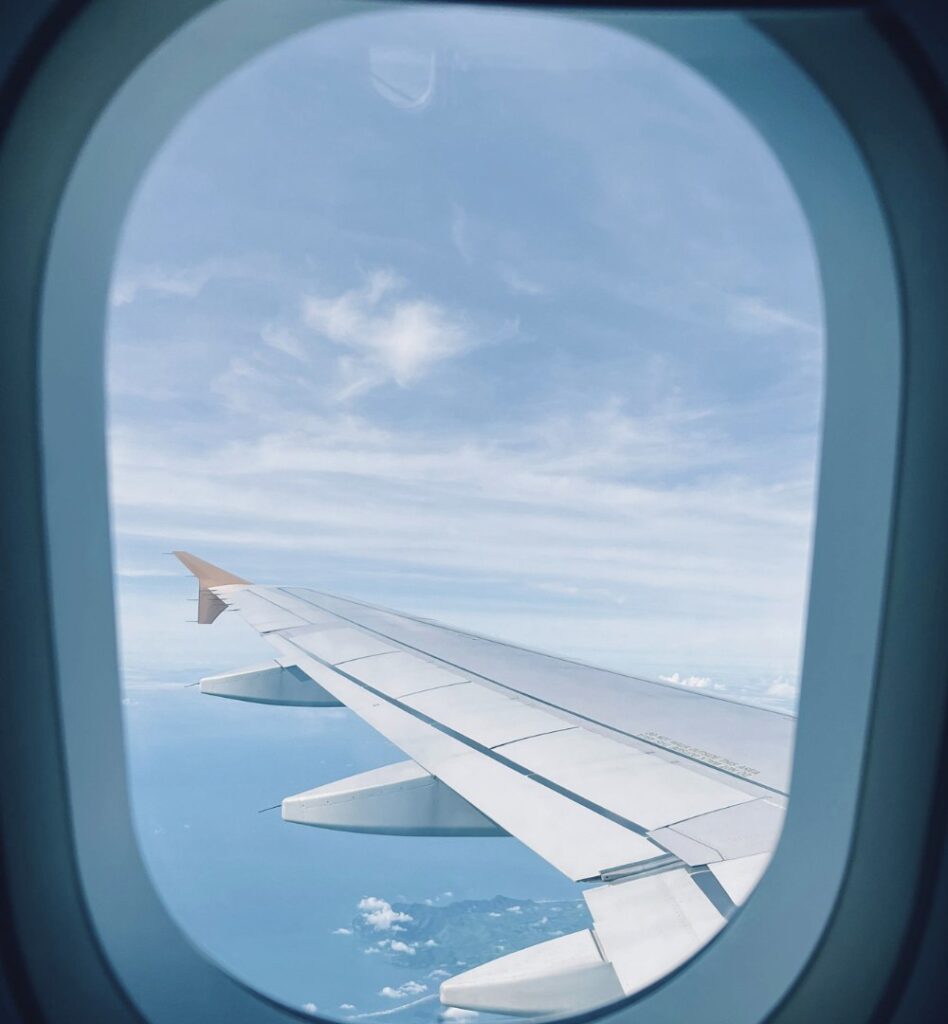 View from an airplane window showing the wing over a deep blue sea and scattered Greek islands under a bright sky.