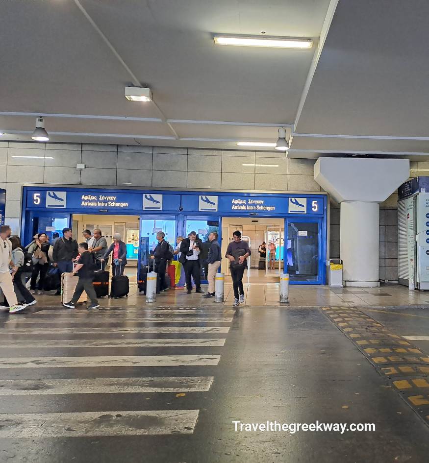Travelers with luggage walking through the "Arrivals Intra Schengen" Gate 5 at Athens International Airport.