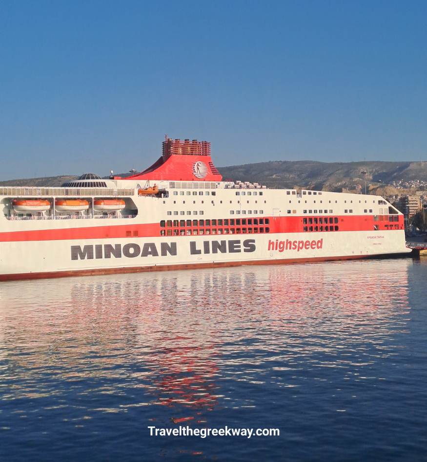 Side view of a large white and red Minoan Lines high-speed ferry docked in the blue waters of a Greek port.
