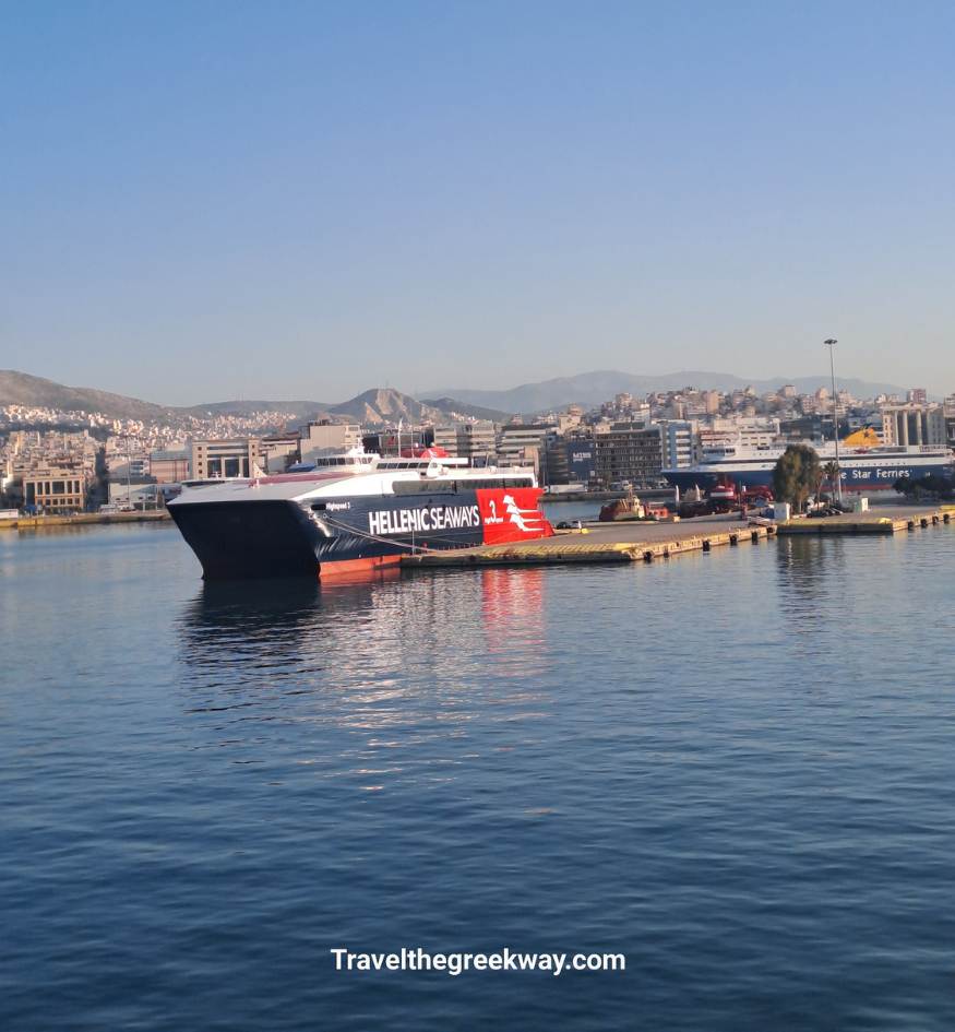 A large blue and red Hellenic Seaways high-speed ferry docked at the Greek port of Piraeus under a clear blue sky.