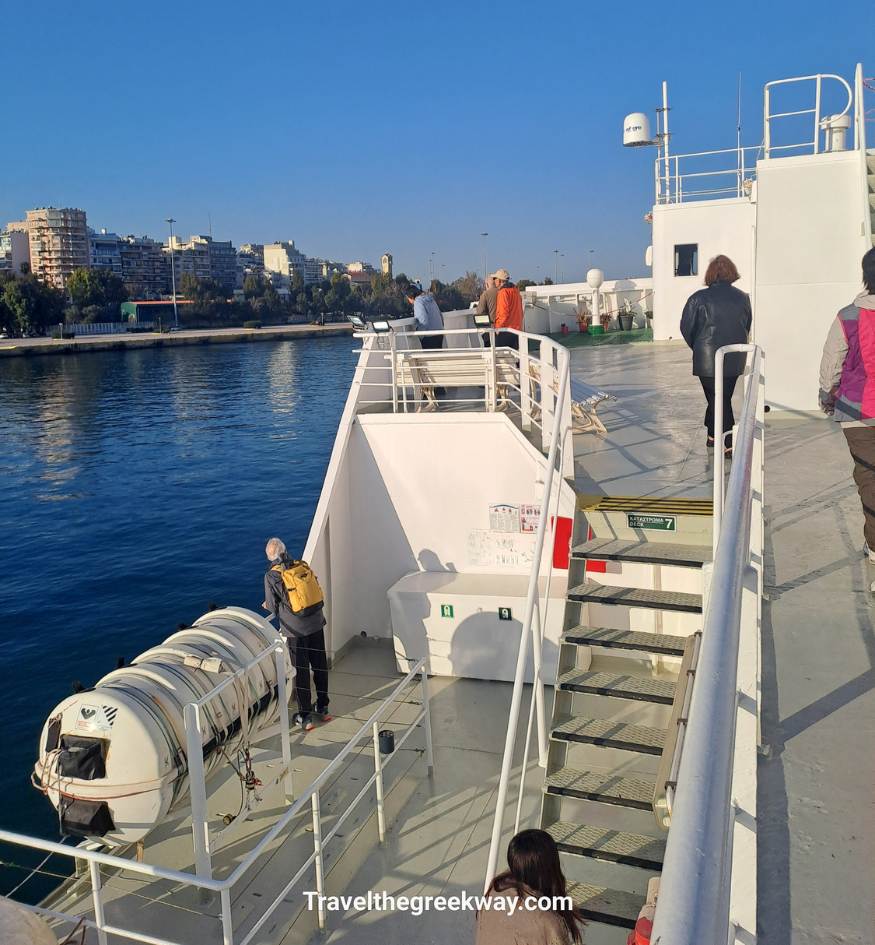 Passengers on the deck of a ferry departing from Piraeus port with the Athens city skyline in the background, Greece.