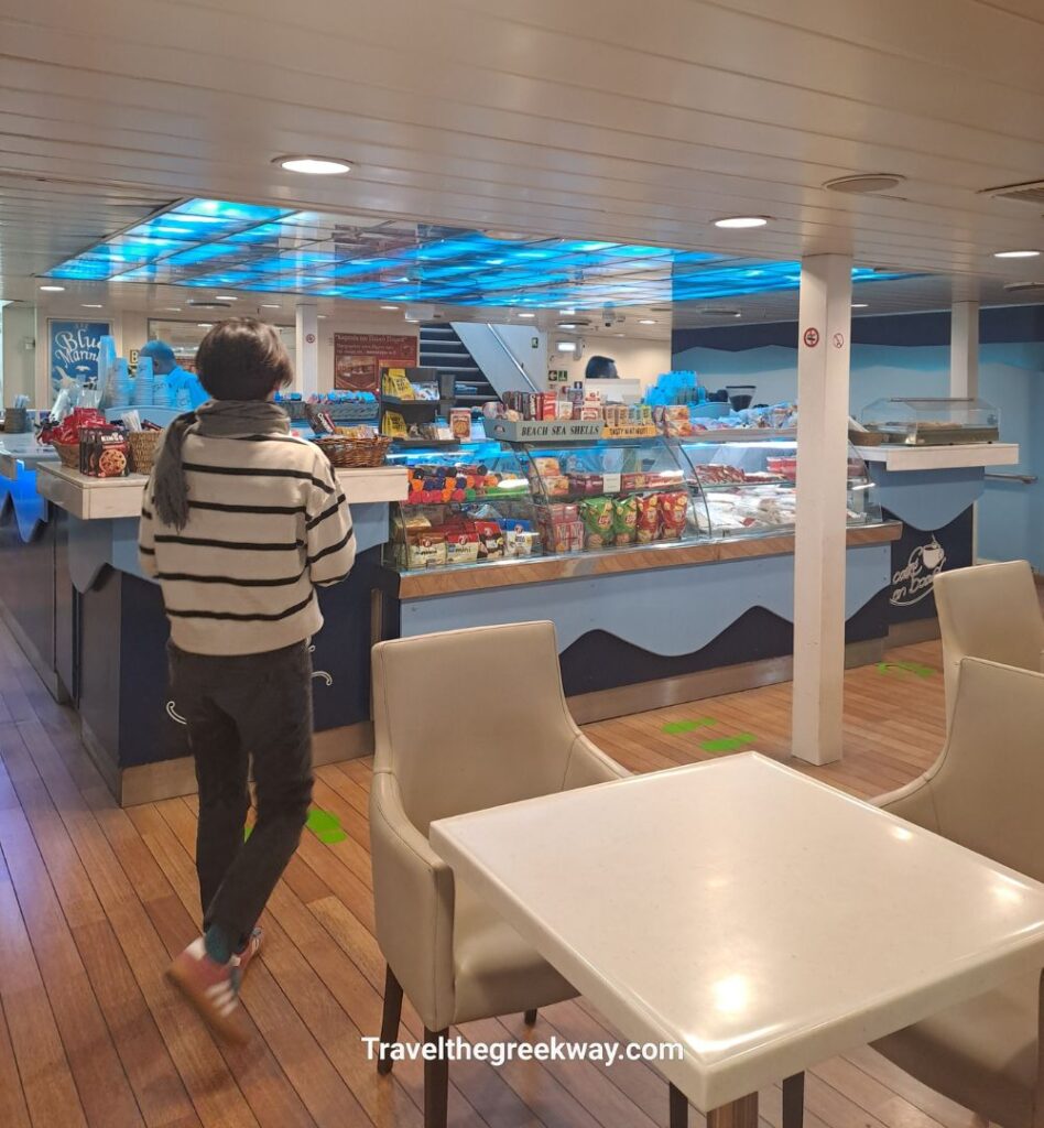 Inside a ferry café with snacks, drinks, and seating area as a passenger browses the counter.
