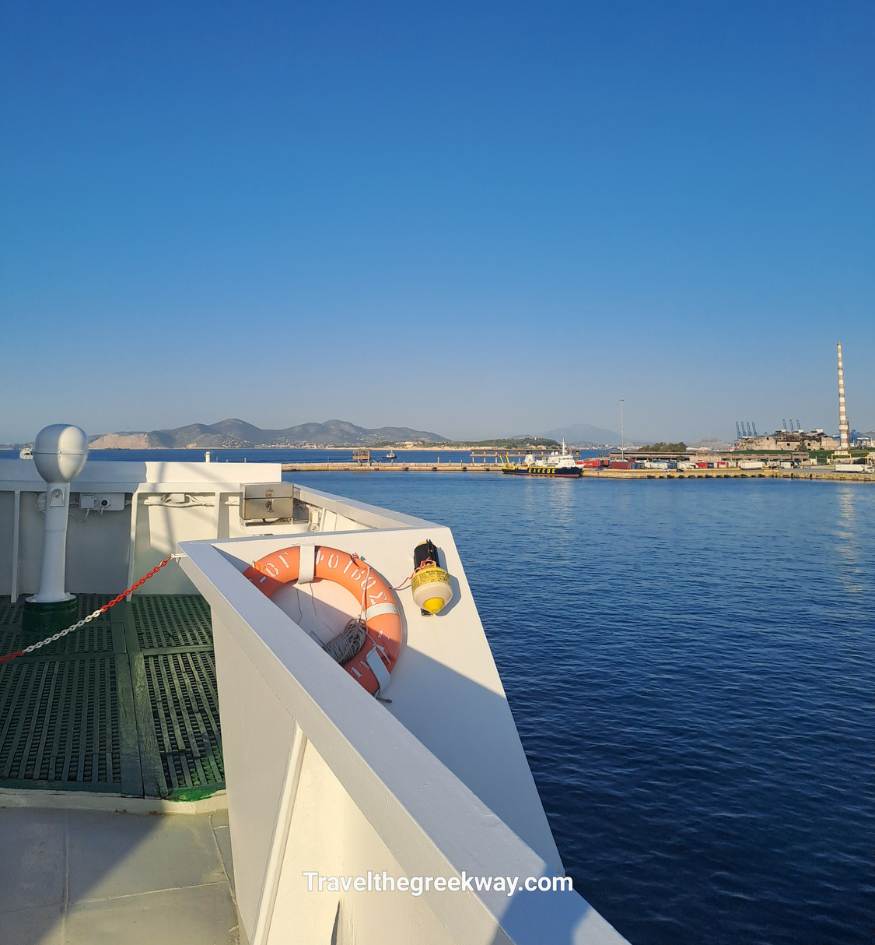 View from ferry deck near Piraeus port, Athens, with calm sea, distant mountains, and industrial harbor in the background.