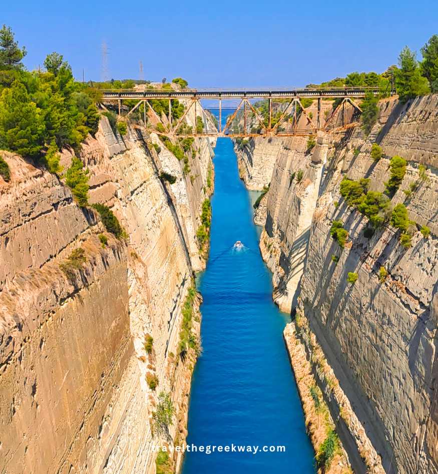A straight-down view of the narrow, turquoise Corinth Canal with steep limestone walls and a bridge crossing the top, Peloponnese Greece.