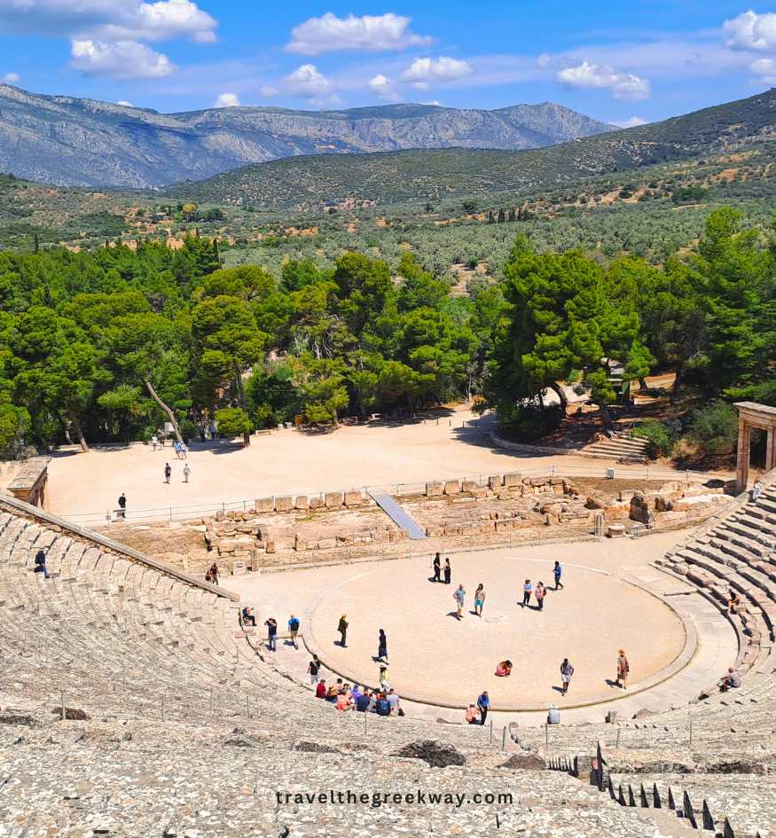 Wide shot of the massive stone Ancient Theater of Epidaurus, in the Peloponnese, Greece, surrounded by lush green trees and rolling Greek mountains.