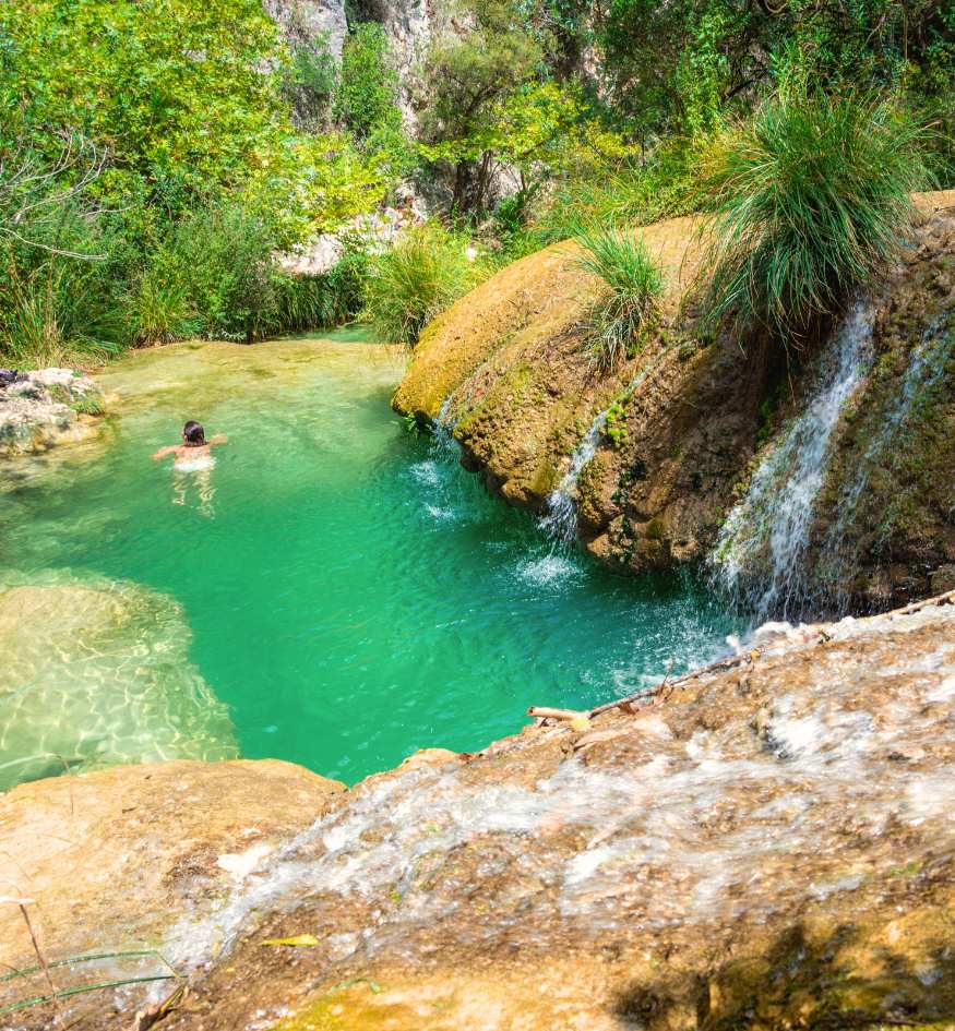 A hidden emerald green lake and cascading waterfall at Polylimnio, a lush natural paradise in Messenia, Peloponnese.