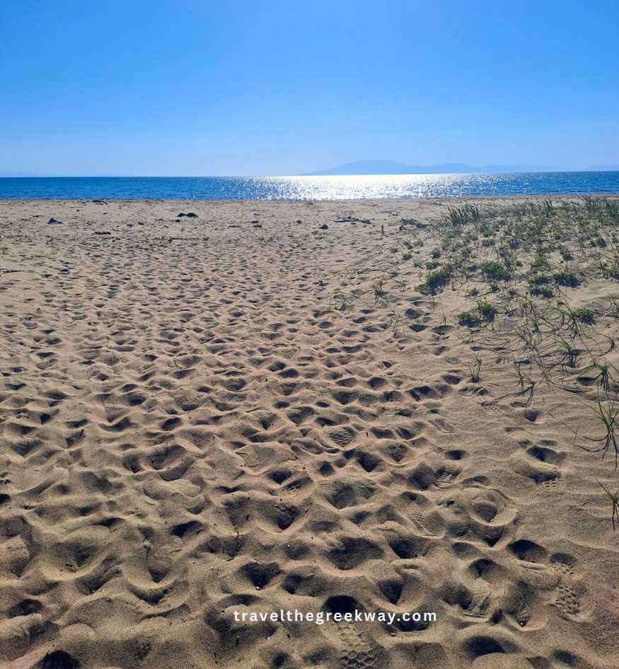 Sandy beach of Kalogria in the Peloponnese with footprints and a birght blue sea and sky.