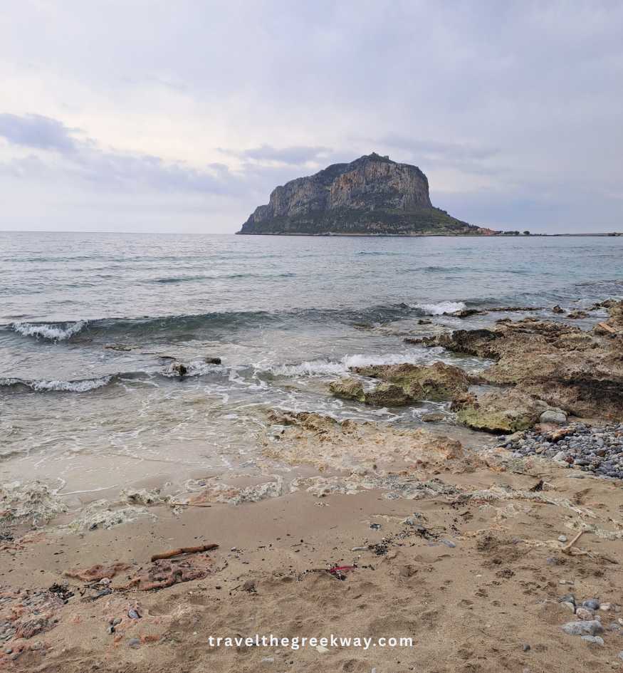 Sandy and rocky shore overlooking the massive rock of Monemvasia, Peloponnese Greece.