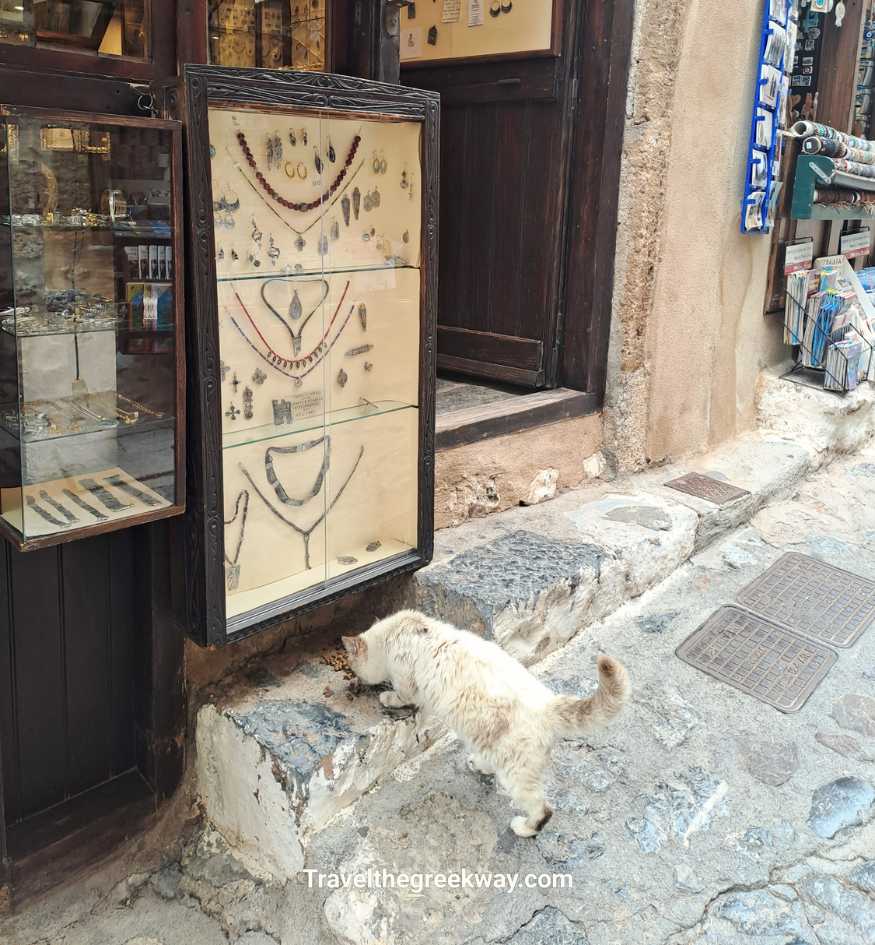 A local cat exploring a stone path next to a jewelry display in Monemvasia, Peloponnese Greece.