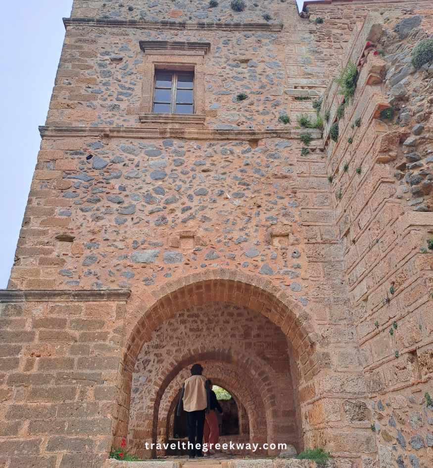 Tourists walking through an old stone fortress gate inside Monemvasia, Peloponnese Greece.