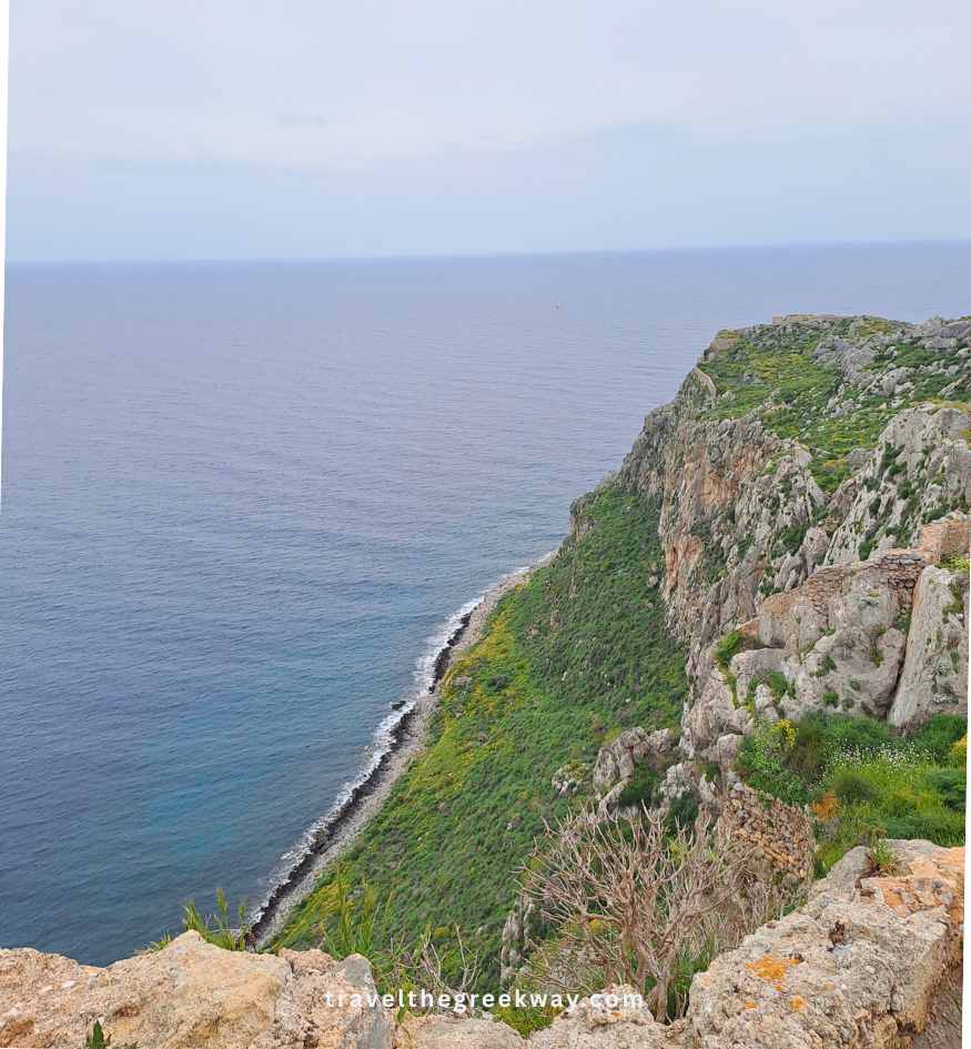 Steep, green cliffside overlooking the vast blue Myrtoan Sea in Monemvasia, Peloponnese Greece.
